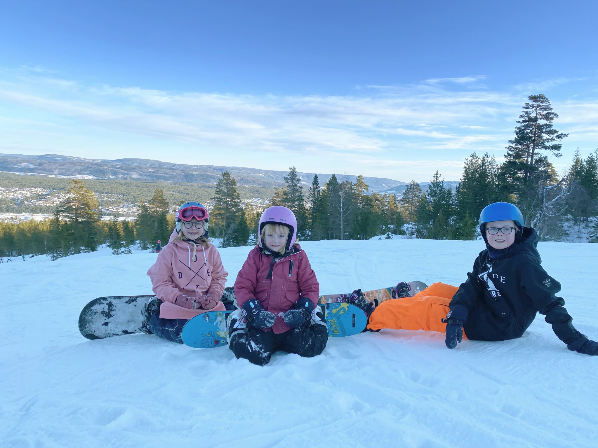 Barn på sitter i alpinbakken med snowboard